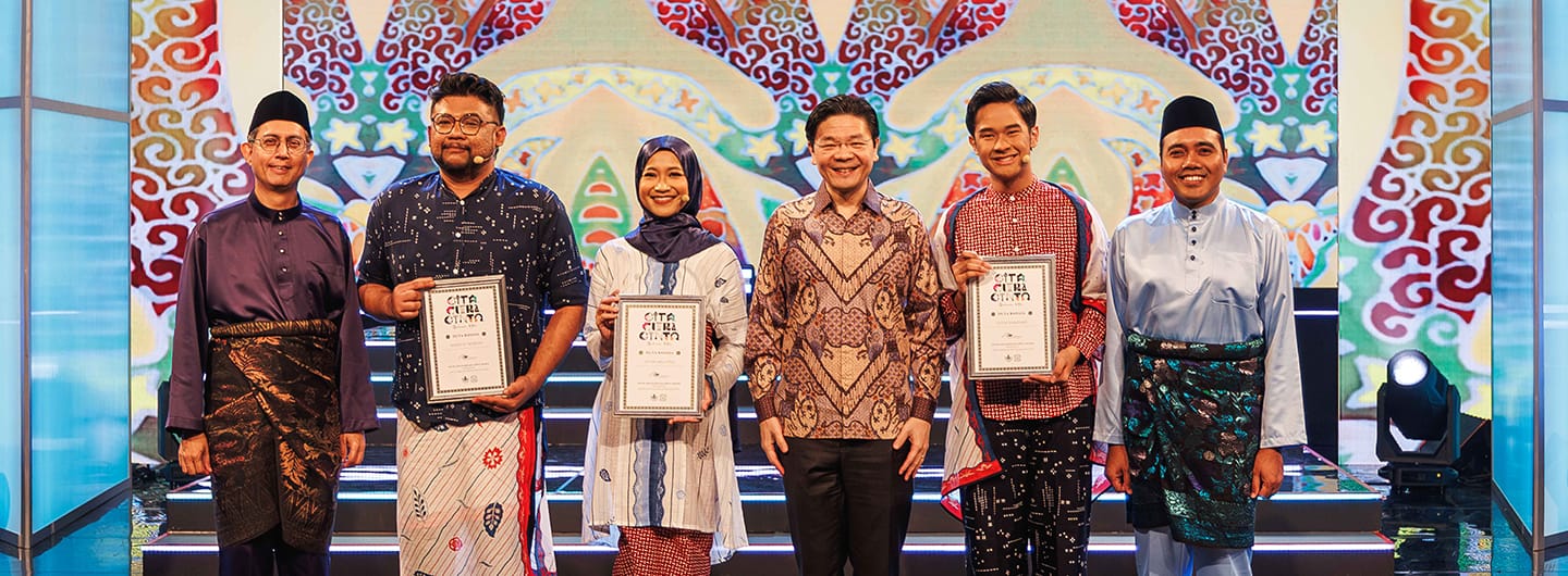 Six people in traditional attire holding framed certificates on stage.